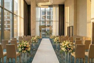 A beautifully decorated wedding venue with elegant floral arrangements and a white aisle leading to a charming archway under soft lighting.
