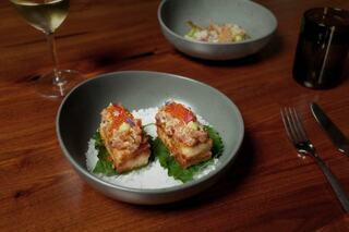 Two elegant bite-sized appetizers sit on a bed of salt, garnished with vibrant toppings, accompanied by a glass of white wine in soft lighting.