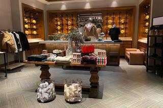 A cozy boutique features clothing displays with warm lighting, a wooden table showcasing garments, and decorative accents, creating an inviting atmosphere.