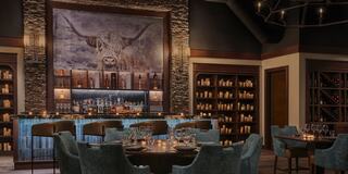 A cozy, upscale dining space features stone accents, a vibrant bar, and elegant seating, illuminated by soft lighting and decorative shelves.