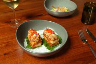 Two elegant appetizers sit on a bed of salt, topped with vibrant garnishes, accompanied by a glass of white wine and a second dish in the background.