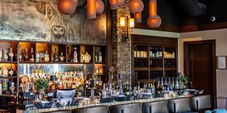 A stylish bar features a stone wall, various bottles on display, and modern pendant lighting, creating an inviting atmosphere.