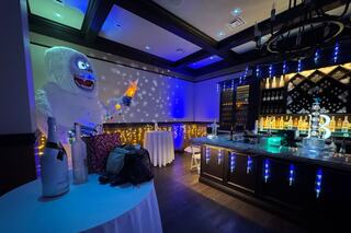A festive bar area featuring blue lighting, a yeti decoration with a star, and elegantly set tables, creating a vibrant party atmosphere.