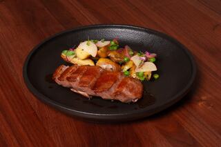 Succulent sliced duck breast served with colorful roasted potatoes, fresh peas, and vibrant herbs on a sleek black plate.