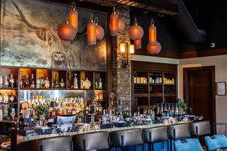 A stylish bar features a striking mural, elegant lighting fixtures, and shelves stocked with various spirits, creating a cozy atmosphere.