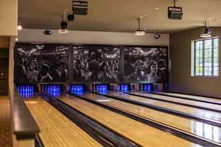 A stylish bowling alley features wooden lanes, colorful pin lights, and vintage black-and-white photos of a lively crowd on the walls.