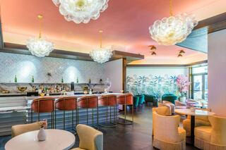 A chic bar area features elegant lighting, stylish seating, and tropical wall decor, creating a vibrant and welcoming atmosphere.