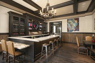 A stylish bar area features a dark wood counter, wine storage, modern stools, and elegant lighting, complemented by a colorful wall artwork.
