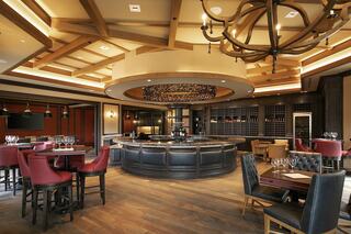 A stylish, modern restaurant features wooden accents, a circular bar, plush seating, and a warm, inviting atmosphere.