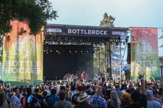 A lively music festival scene with a large crowd enjoying performance on a vibrant stage adorned with colorful banners.