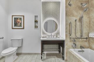 A modern bathroom featuring a circular vanity mirror, textured tiles, a bathtub, and elegant decor, creating a sleek and inviting atmosphere.