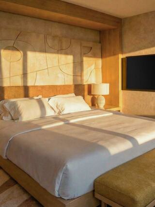 A cozy bedroom features a textured headboard, soft bedding, warm lighting, and a modern TV, creating a serene and inviting atmosphere.