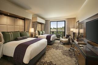 A stylish hotel room features two double beds with elegant linens, a cozy seating area, and a balcony offering scenic views.