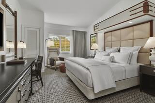 A modern hotel room features a king-sized bed, sleek furniture, a large window, and stylish decor, creating a cozy and inviting atmosphere.