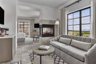 A modern, cozy living room features a gray sofa, a stylish coffee table, and a fireplace, with large windows offering scenic views.