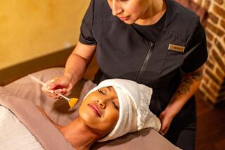 A serene spa scene shows a client receiving a facial treatment, with a therapist applying a product to the client's relaxed face.