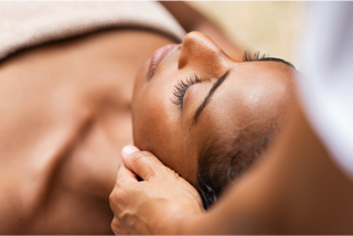 A serene woman receiving a gentle head massage, relaxing with her eyes closed, surrounded by a calming, spa-like environment.