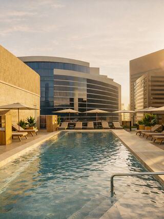 A serene rooftop pool surrounded by modern buildings, featuring lounge chairs and umbrellas, illuminated by warm sunset light.