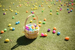 A wicker basket filled with colorful Easter eggs sits on green grass, surrounded by scattered, vibrantly colored eggs.