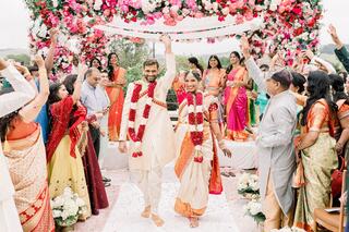 A joyous wedding celebration with a couple in traditional attire, surrounded by family and friends under a floral canopy, filled with vibrant colors.