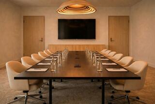 A modern conference room featuring a long table, swivel chairs, water bottles, and a wall-mounted screen under an elegant light fixture.