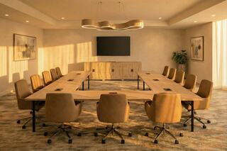A modern conference room features a large wooden table surrounded by ergonomic chairs, illuminated by soft sunlight and minimalistic decor.