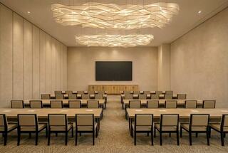 A modern conference room features stylish lighting, rows of tables and chairs, and a large screen at the front, creating an inviting atmosphere.