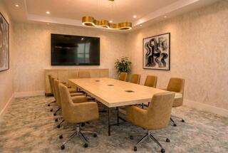A modern conference room features a large wooden table surrounded by tan chairs, a TV, and abstract art on the walls.