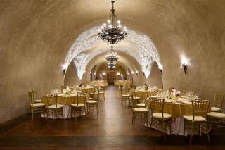 An elegantly lit banquet hall features golden tables, plush seating, and ornate chandeliers, creating a warm, inviting atmosphere for gatherings.
