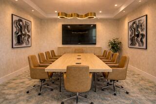 A modern conference room features a long wooden table, ergonomic chairs, abstract wall art, a large screen, and a potted plant.