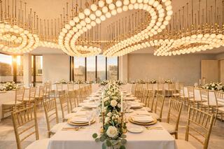 A stunning banquet hall with elegant decor, golden chairs, and a dramatic chandelier, bathed in warm sunset light.