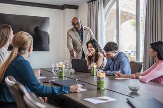 A diverse group of professionals engages in a meeting, with one person presenting while others listen and interact around a conference table.