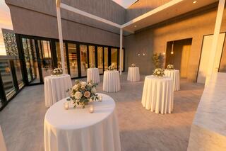Elegant outdoor venue featuring round tables with white tablecloths, floral centerpieces, and soft lighting, set against a modern backdrop.