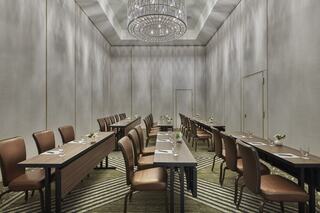 A sleek conference room features elegant wooden tables and brown chairs, with a chandelier overhead and soft lighting for a professional setting.