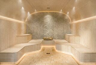 A serene steam room features curved stone benches, soft lighting, and a calming stone centerpiece, creating a tranquil atmosphere.