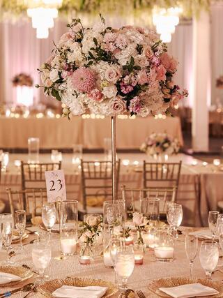 An elegant banquet setting features tall floral centerpieces, soft lighting, and beautifully arranged tables, creating a romantic ambiance.