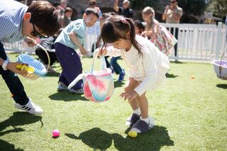 Children participate in an outdoor egg hunt, collecting colorful eggs in baskets on a sunny day. Joyful laughter fills the atmosphere.