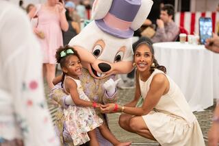 A joyful little girl and her mother pose with a costumed bunny character, capturing a fun moment at a festive event.