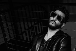 A stylish man with a beard wears trendy oversized sunglasses and a leather jacket, posing confidently in a moody black-and-white setting.