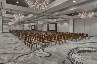 A large conference room with rows of brown chairs, modern lighting fixtures, and a large screen at the front, ready for an event.