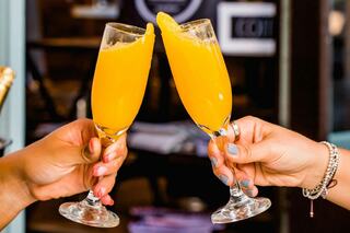Two glasses of orange mimosa clink together, celebrating a joyful moment. It's bright, bubbly, and full of anticipation.