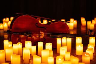 A cello rests among glowing candles, creating a warm and serene atmosphere, evoking a sense of tranquility and reflection.