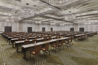 A spacious conference room features multiple rows of tables and chairs, elegant chandeliers, and a modern carpet design, ideal for events.