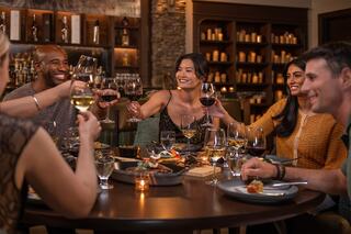 A group of friends joyfully toasts at a dinner table filled with delicious food and drinks, celebrating together in a cozy setting.