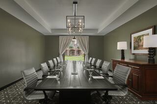 A modern conference room features a long table, executive chairs, elegant decor, and large windows with curtains, creating a professional atmosphere.