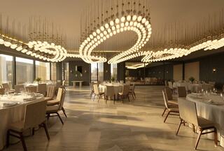 A spacious, elegant dining area featuring round tables, soft lighting from modern fixtures, and a sophisticated atmosphere with muted colors.