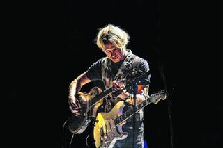 A musician passionately plays multiple guitars on stage, illuminated by dramatic lighting, showcasing talent and intense focus.