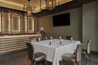 A modern dining space features a square table with chairs, bottles of water, and stylish lighting, complemented by a sleek bar area.