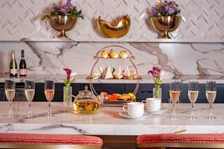 A stylish setting features a tiered dessert stand with colorful treats, tea, and champagne flutes, accented by floral arrangements.