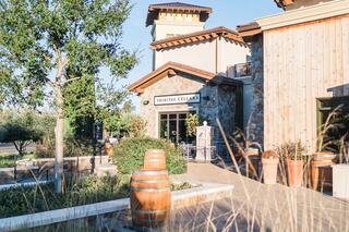A charming winery entrance features rustic stone and wood architecture, surrounded by greenery and decorative barrels.